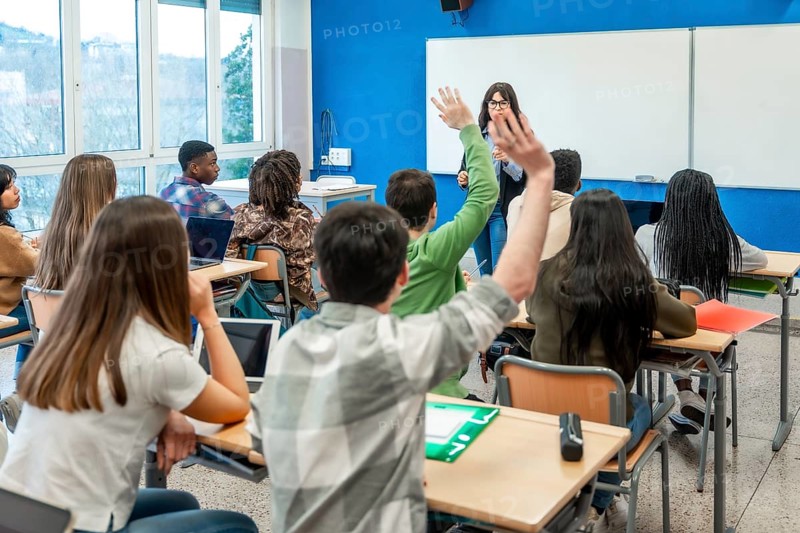 Diverse group of teenage high school students raising hands to answer teacher's question during class