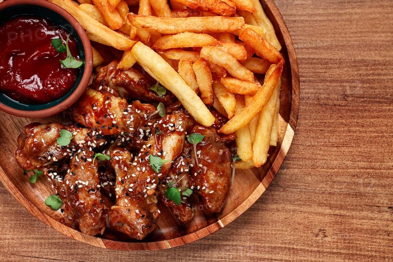 Barbecue chicken wings, sprinkled with sesame seeds, with French fries, and sauce, on a wooden plate, rustic style