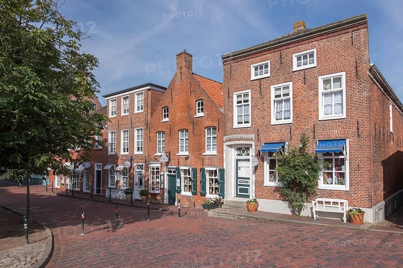 Brick houses along a cobbled street in sunny weather, historic town centre with trees and windows, cheerful atmosphere, fishing village Greetsiel, Krummhörn, East Frisia, Lower Saxony, Germany