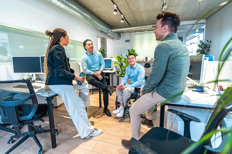 Businesspeople having a discussion in a modern office, with a colleague using a wheelchair, demonstrating workplace inclusivity