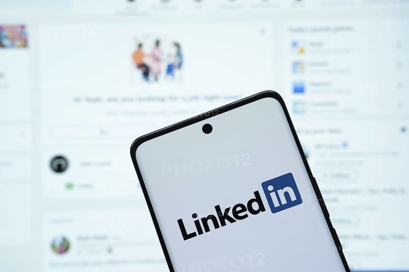Dhaka, Bangladesh - 17 March 2025: The logo of the linked in is displayed on a smartphone screen, and the website linked in is visible on a computer screen in the background
