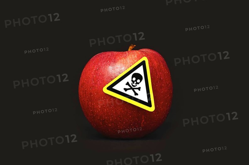 Concept for pesticide residues in agricultural food products dangerous to humans. A red apple with poison symbol sticker on black background