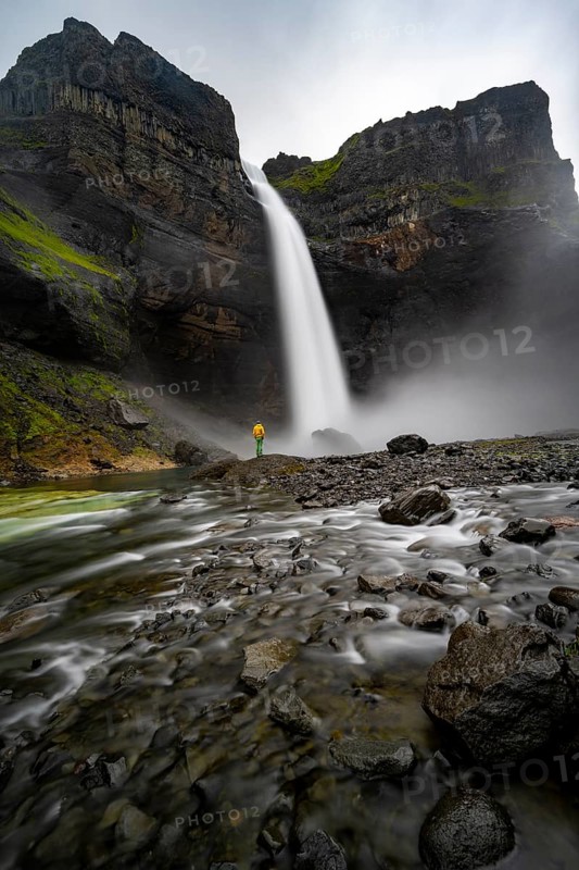 Young man with yellow jacket standing in front of waterfall, Haifoss and Granni waterfall at a canyon, Fossá í Þjórsárdal, with river í Þjórsárdal, long exposure, dramatic landscape, Hekla, Iceland