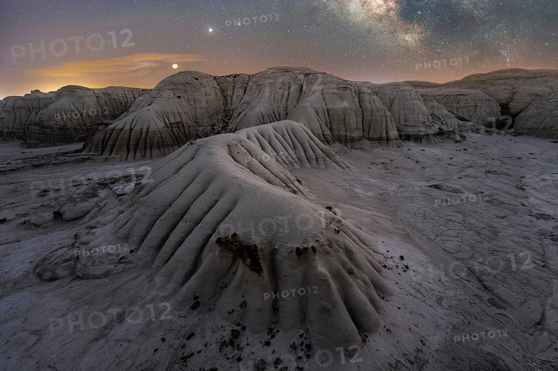 A serene nighttime scene captures Utah's textured landscape under a starlit sky, highlighted by the moon and distant planets