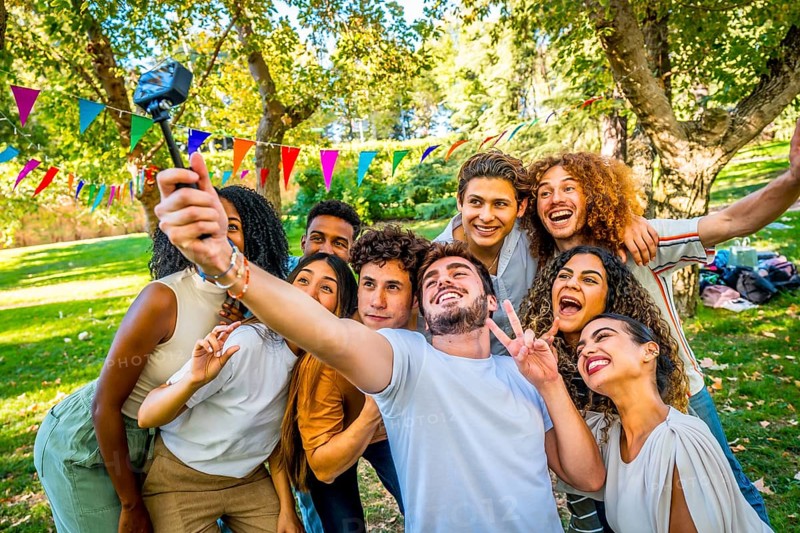 Cool multi-ethnic friends gesturing happily taking selfie in a park celebrating picnic party