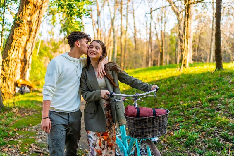 Romantic couple enjoying a leisurely stroll in a park with their bicycle, sharing a tender kiss amidst the beauty of nature