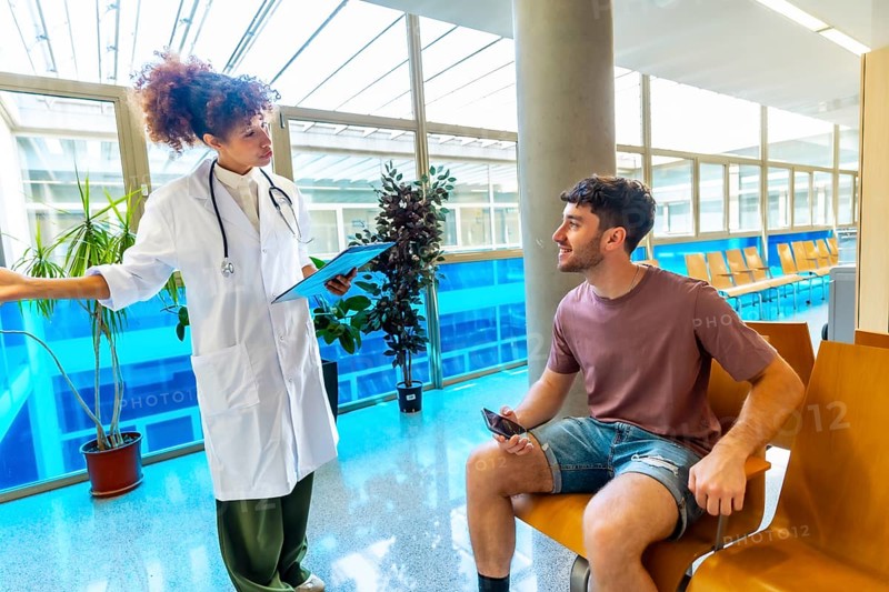 Doctor holding a clipboard, discussing diagnosis with a patient seated in a waiting area, fostering communication in a healthcare setting