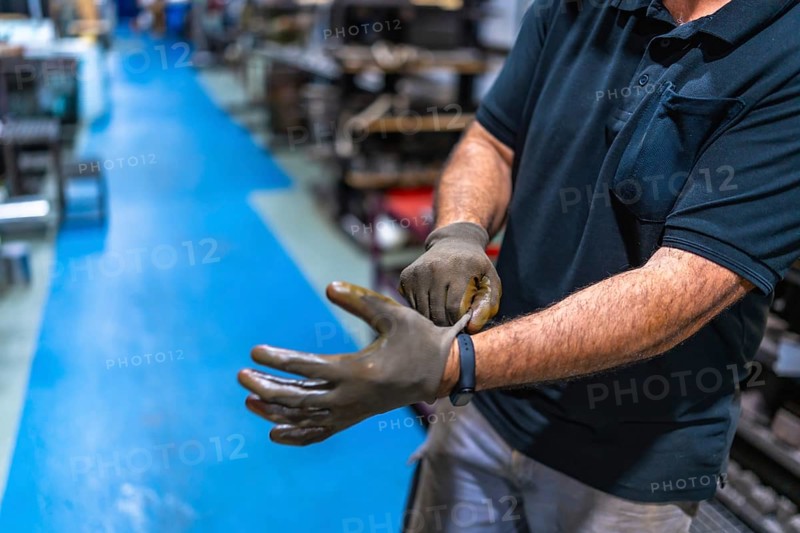 Cropped photo of a part of an unrecognizable caucasian man putting on protective gloves in a metallurgic factory