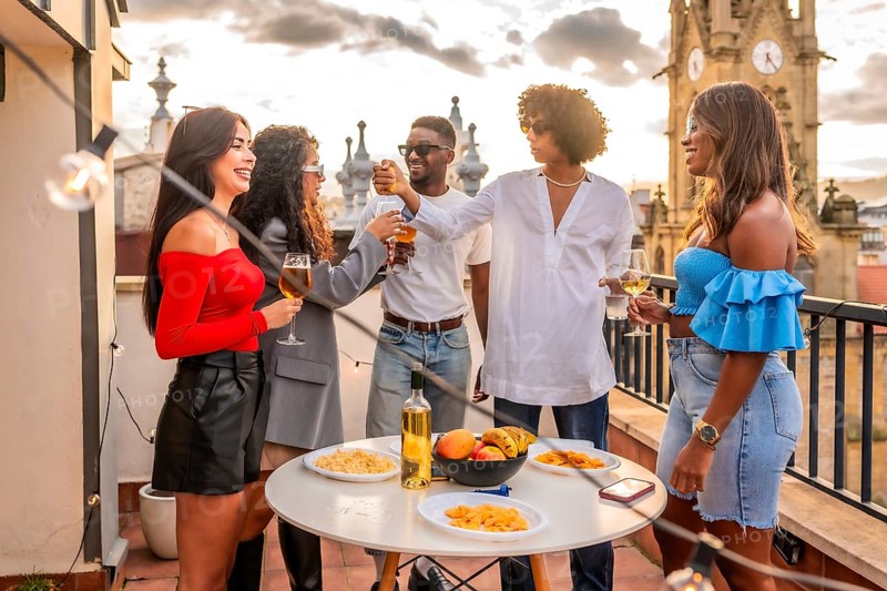 Multi-ethnic males and females friends eating snacks and beverages on a rooftop during sunset