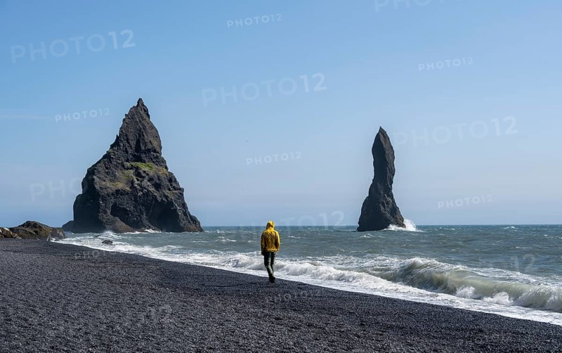 Tourist on black beach, rock Reynisdrangar in water, at Reynisfjara beach, Vik, South Iceland, Iceland