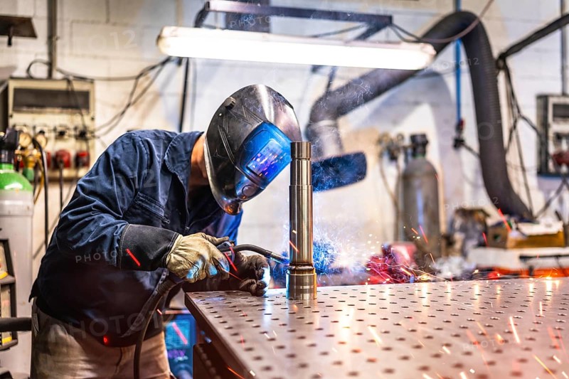 Three quarter length photo of a welder with facial mask and safety work wear working in factory