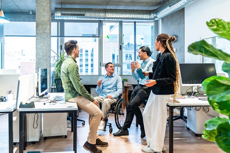 Businesspeople having a conversation in a modern office, demonstrating inclusion and teamwork with a colleague using a wheelchair