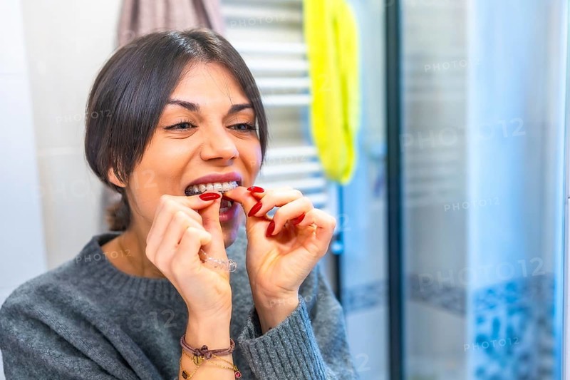 Woman putting on modern transparent dental aligner in the bathroom