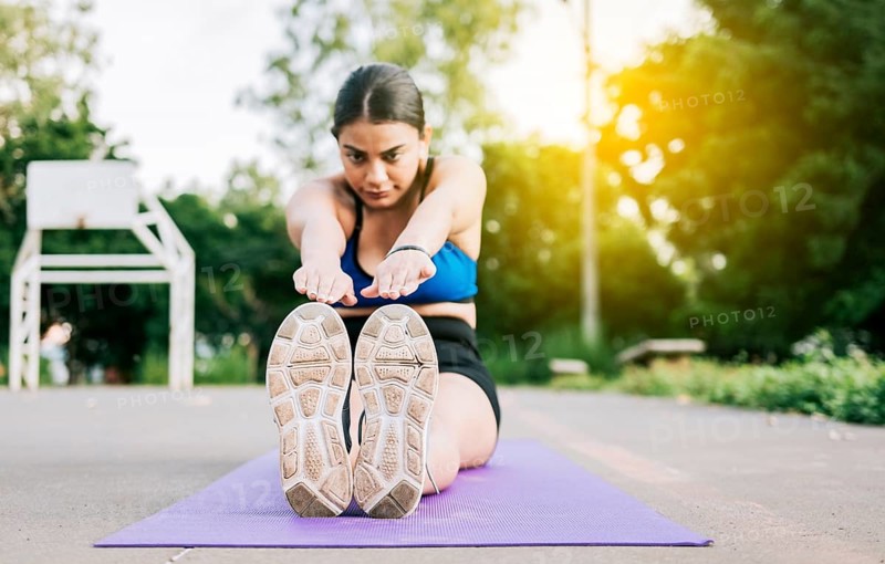 Athlete woman sitting doing leg stretch in a park. Athlete girl sitting on a mat stretching her legs in a park, Sporty girl stretching her legs sitting on a mat in a park, Managua, Nicaragua