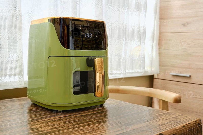 Preheating an air fryer on a wooden table in a well-lit kitchen. Sunlight streams through a curtain, creating a warm atmosphere for cooking and meal preparation