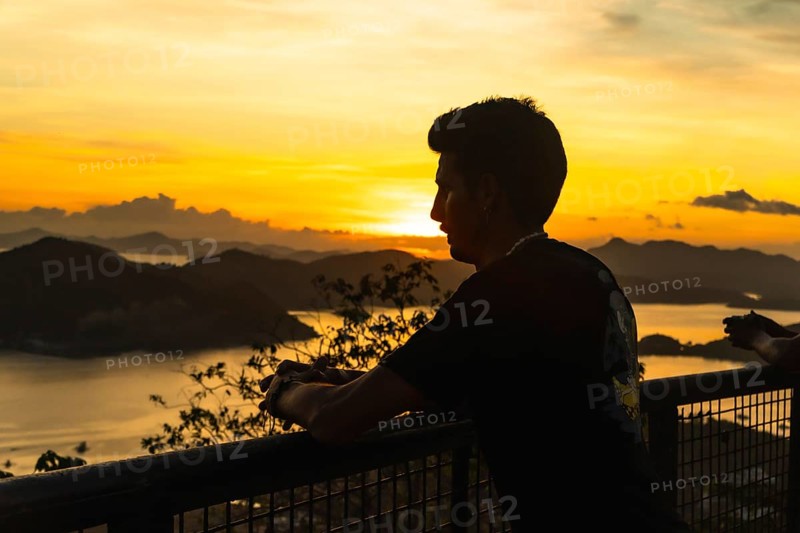 Silhouette of a tourist leaning on a railing, admiring the breathtaking golden sunset over coron island's picturesque landscape in the philippines