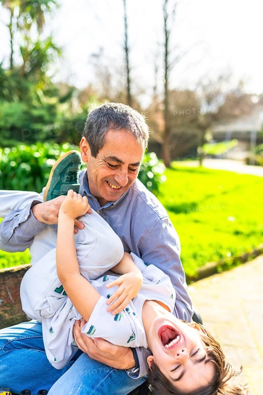 Grandfather and grandson enjoying a playful moment in the park, tickling and laughing together