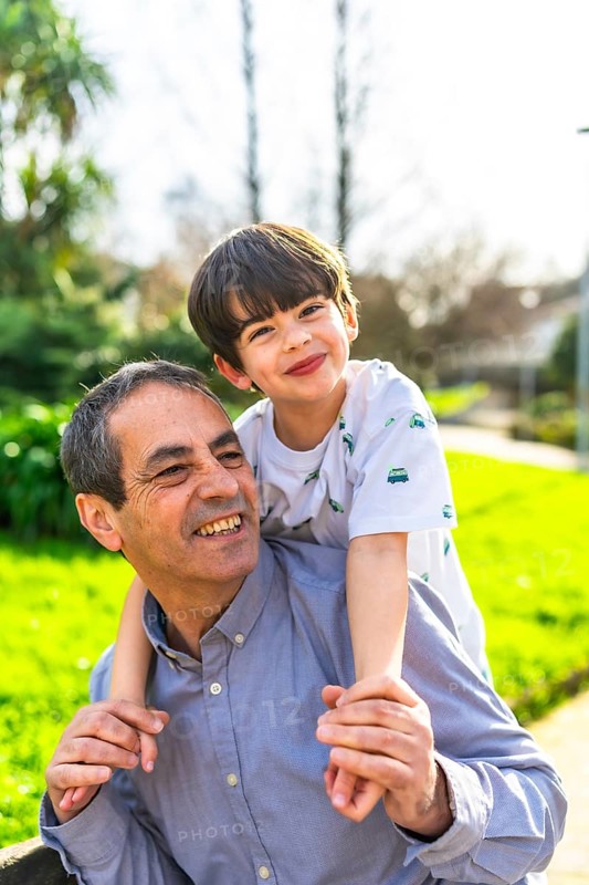 Grandfather giving piggyback ride to his grandson in a park, smiling and enjoying a sunny day together