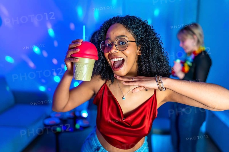 Cheerful young woman enjoying nightlife, holding a fancy beverage and dancing with friends in a vibrant nightclub