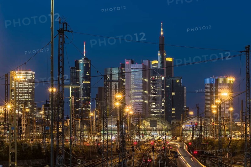 View over rails and moving train to the luminous main station, in the background the colourful shining skyline of Frankfurt am Main at blue hour, Gallusviertel, Frankfurt am Main, Hesse, Germany