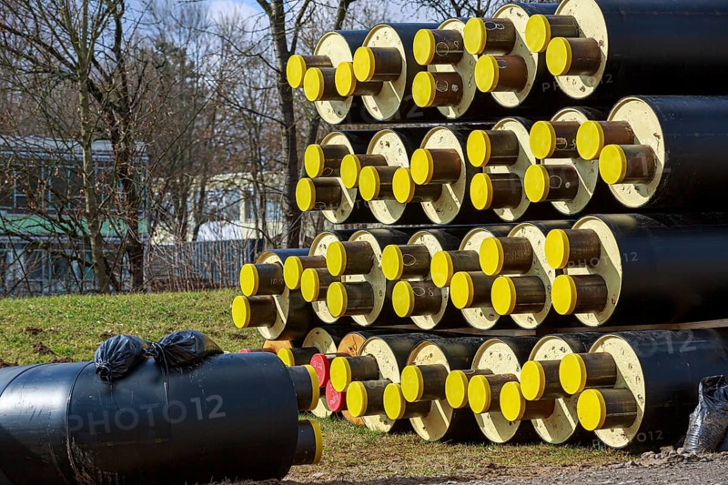 Stacked district heating pipes with yellow ends lie piled up in a meadow