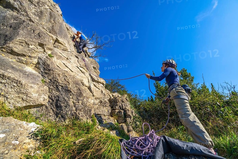 Two female climbers ascending a rock face, one belaying the other, ensuring safety during their outdoor rock climbing adventure
