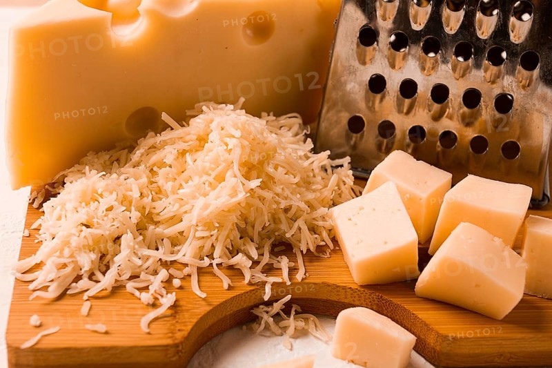 Geriebener Käse, Maasdam, auf einem Schneidebrett, Reibe und Käsemesser, Nahaufnahme, keine Personen