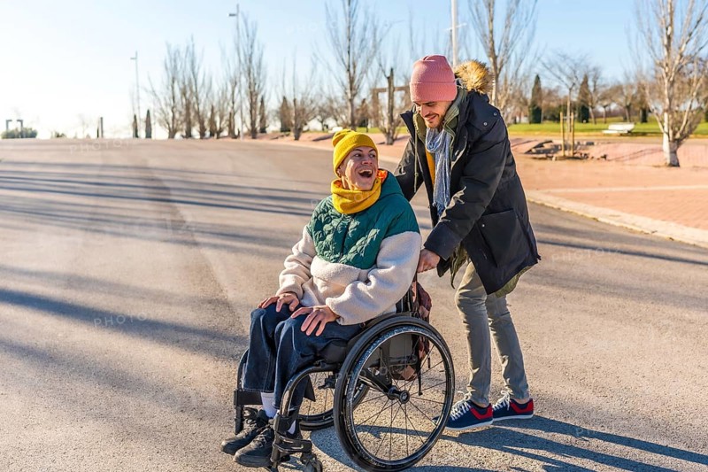 Young caregiver assisting a happy senior woman in a wheelchair, enjoying a sunny winter day together in a park
