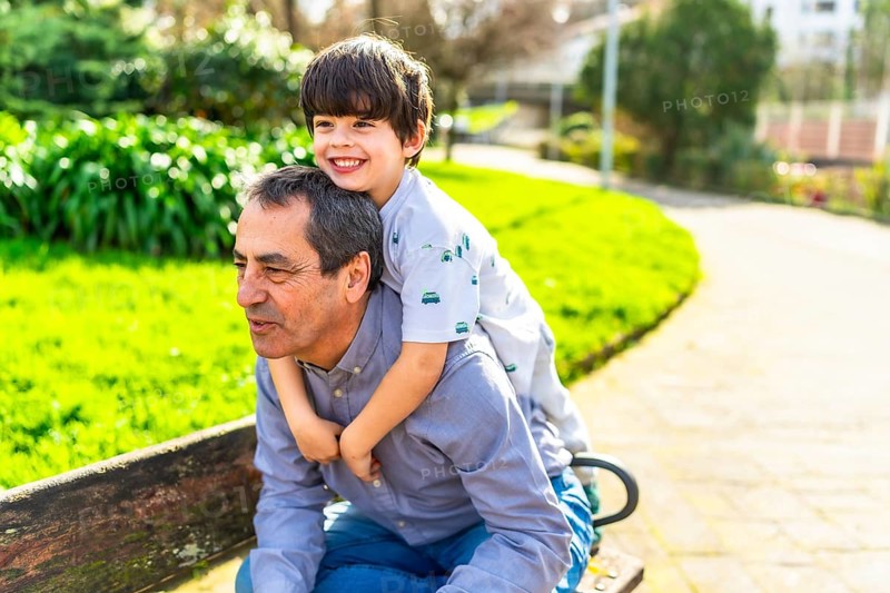 Grandfather giving his grandson a piggyback ride in a sunny park, enjoying a playful moment together
