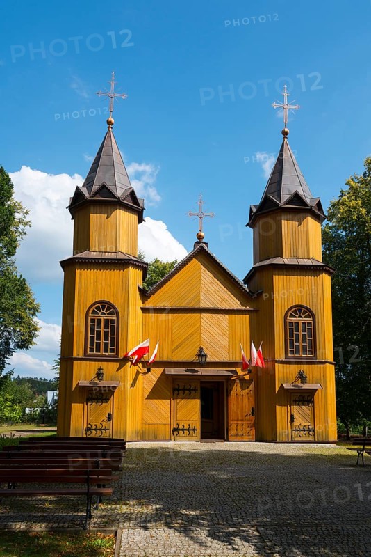 Front view of a wooden church with towers, Polish flags, surrounded by trees and blue sky, wooden church of St Mary Magdalene, Mikaszówka, Mikaszowka, Powiat Augustowski, Podlaskie Voivodeship, Poland