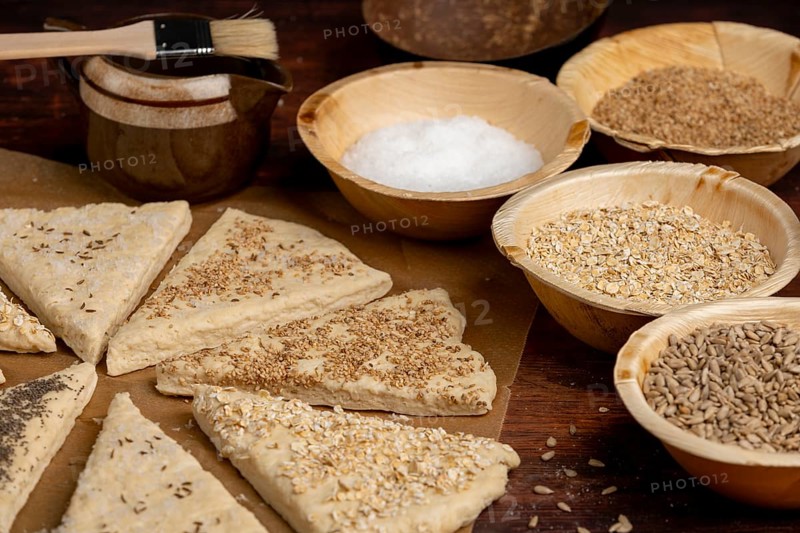 Triangles of dough, sprinkled with various grains and salt, on a rustic wooden table