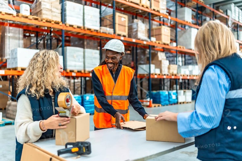Three happy multi-ethnic workers preparing parcels to deliver in a warehouse