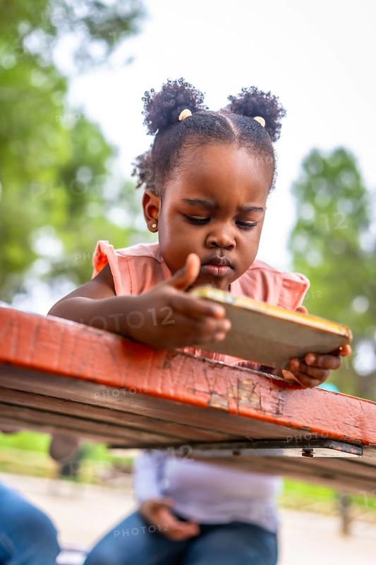 African little girl focus on the screen of a mobile in a park. Addiction concept