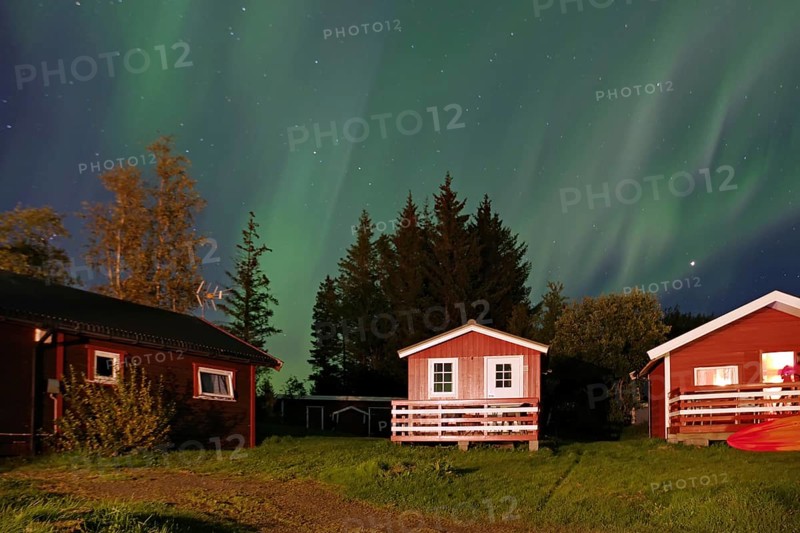 Small, red wooden holiday cabins, northern lights (aurora borealis) cover the sky, Alstahaug, coastal road 17, Nordland, Norway
