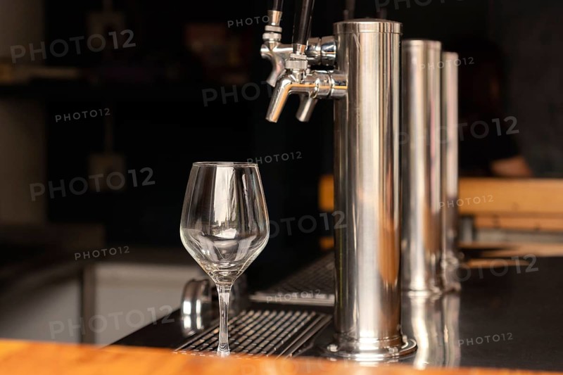An empty glass cup next to a beer tap at the bar of a bar, ready for use. The set reflects a modern and clean bar environment