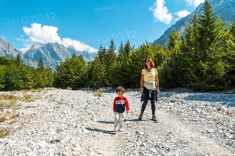 A tourist with her son walking on the Valbona Valley trail next to trees, Theth National Park, Albanian Alps, Albania