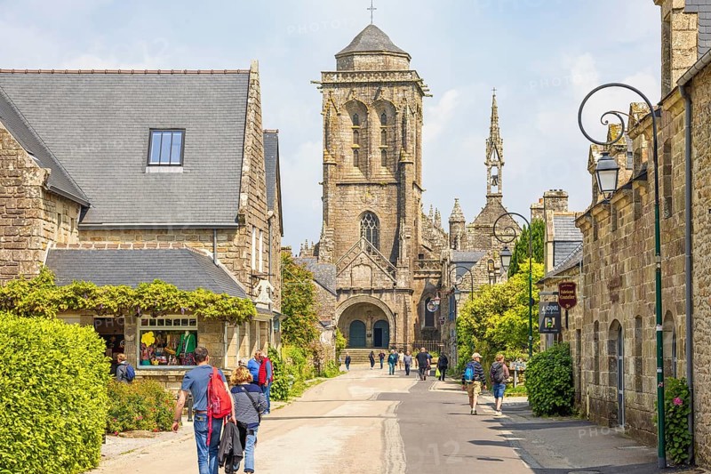 Tourists walking on a street in an old picturesque town with a church and stone houses a summer day, Locronan, Bretagne, France