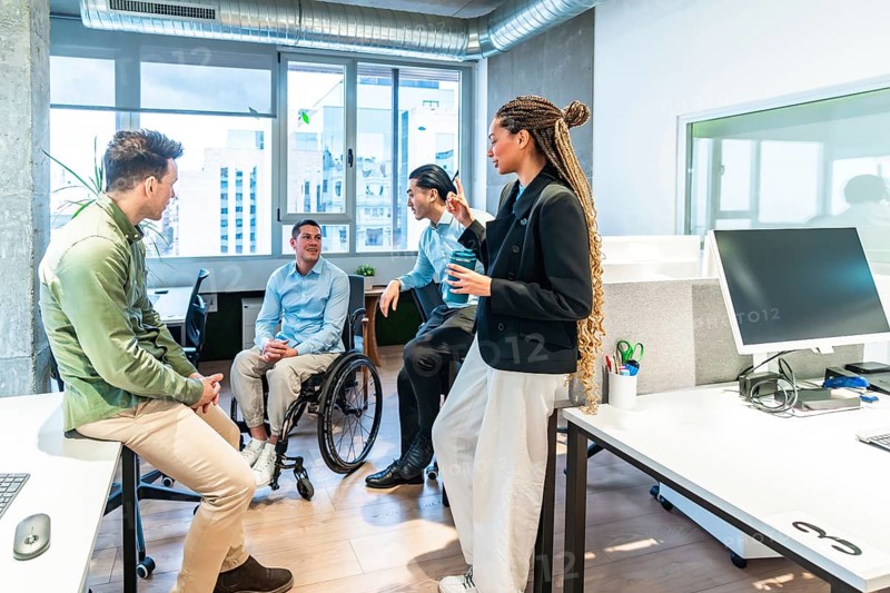 Businesspeople collaborating in a modern office, demonstrating inclusion and teamwork with a colleague using a wheelchair, during a productive workday