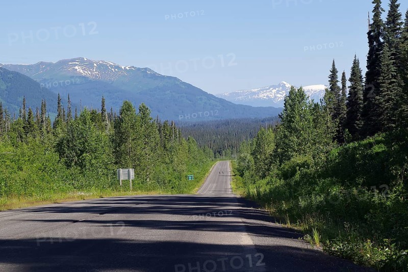 Narrow, traffic-free road leads as endless grades through rugged mountain landscape, forest and snow-covered mountains, wilderness, Stewart Cassiar Highway, British Columbia, Canada
