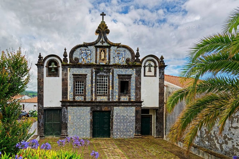 Historic church Convent of Caloura with typical tile pattern, blue and white façade and religious symbols. Exterior view with cloudy sky and garden, Caloura fishing village, Ribeira Chã, Sao Miguel Island, Azores, Portugal
