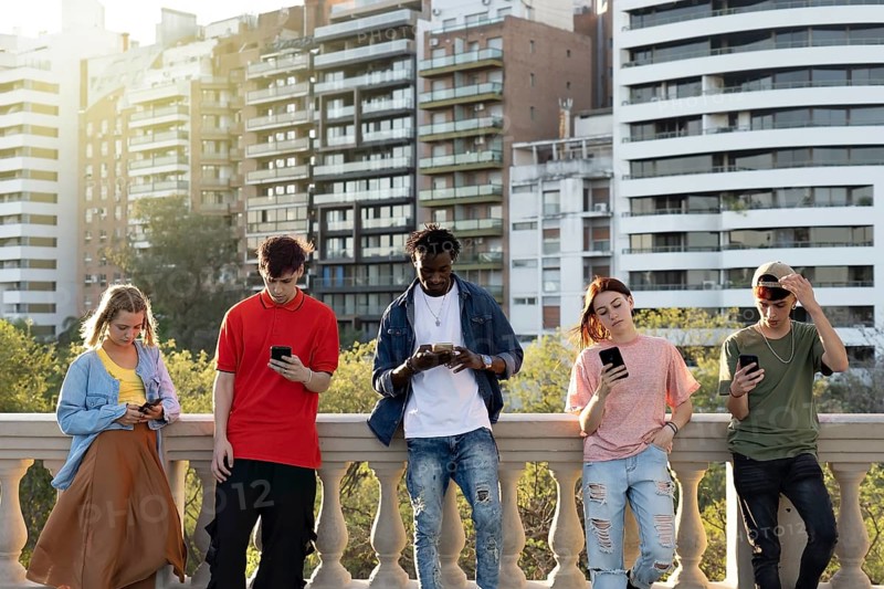 Young people looking down at cellular phone. Teenagers leaning on a wall and texting with their smartphones. Concepts about technology and global communication
