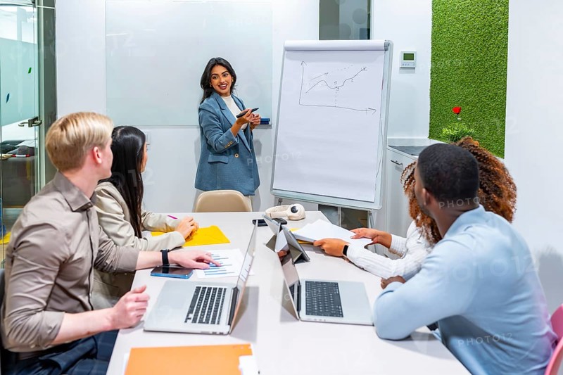 Indian businesswoman using whiteboard to explain positive data to colleagues in a modern office