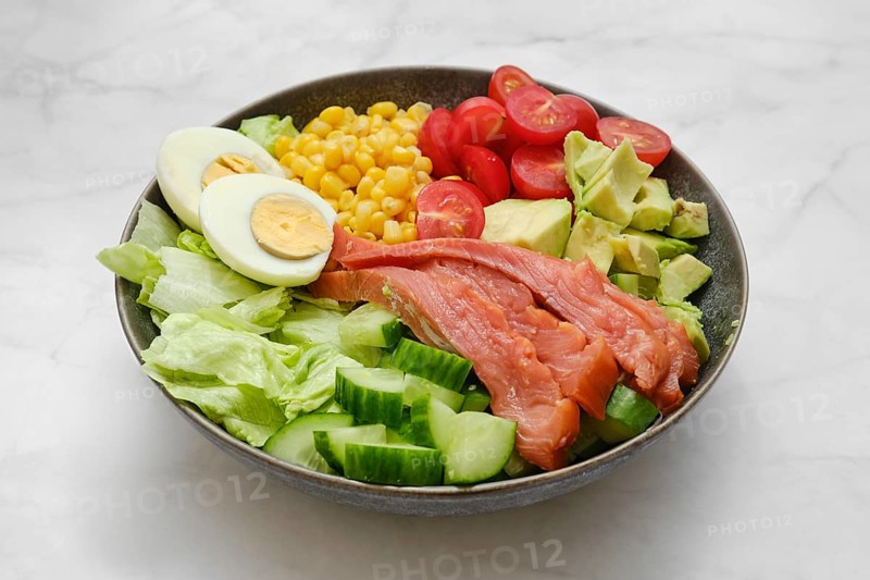 A poke bowl with iceberg lettuce, smoked salmon, boiled eggs, sweet corn, cherry tomatoes, and diced avocado