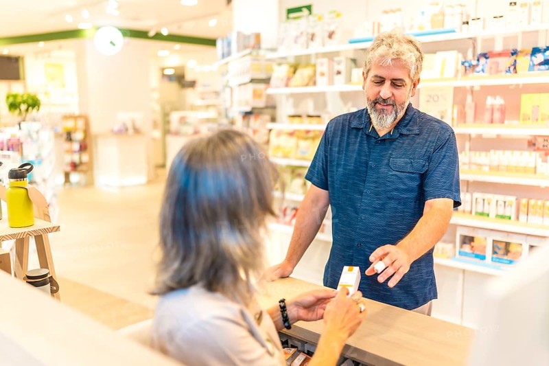 Rear view of a female mature pharmacist assisting a customer in the counter