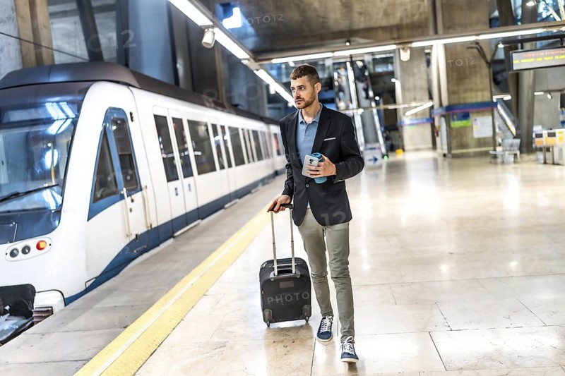 Young businessman walking at the subway station with his suitcase and coffee, going to work