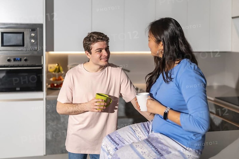 Multiethnic couple enjoying a cozy moment together, sipping coffee in their modern kitchen, sharing smiles and conversation on a relaxing weekend morning