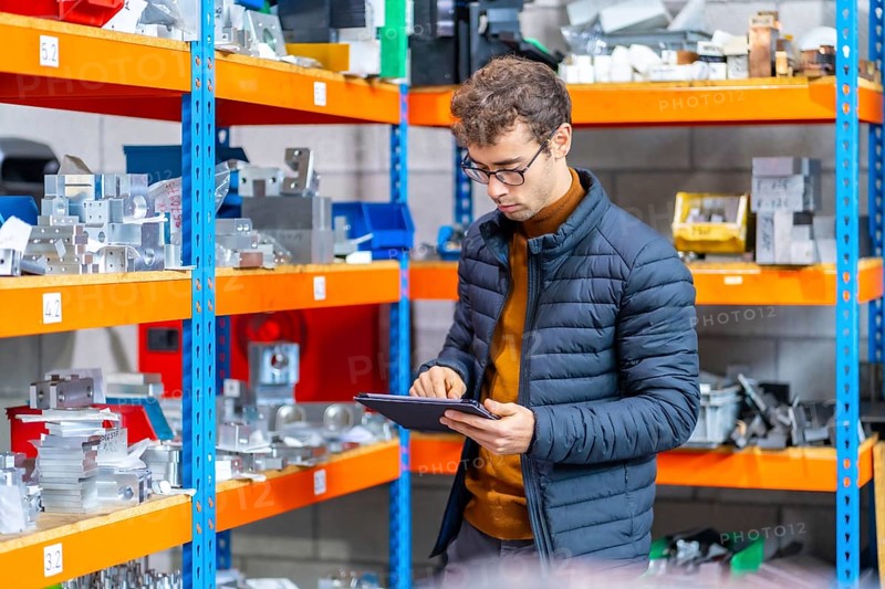 Young male engineer concentrated using tablet in the warehouse of a cnc factory