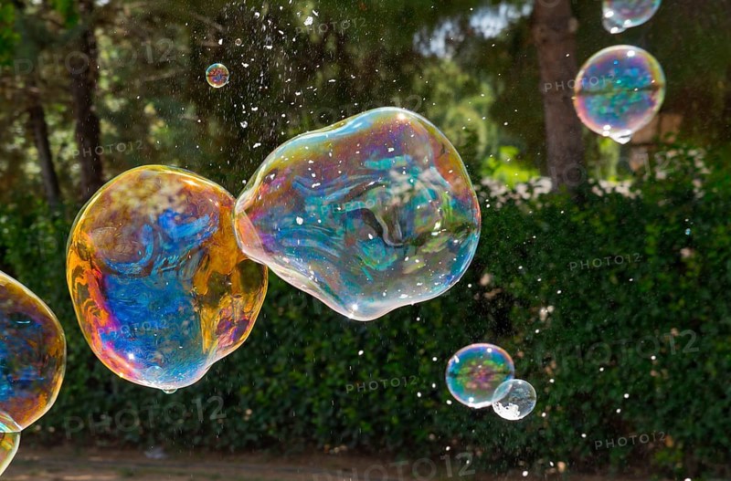 Colourful soap bubbles float in front of a green hedge in nature, Spain