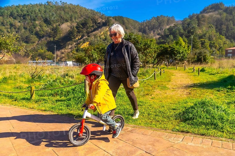 Grandmother teaching her grandson how to ride a balance bike in a sunny park, promoting intergenerational bonding and outdoor activities