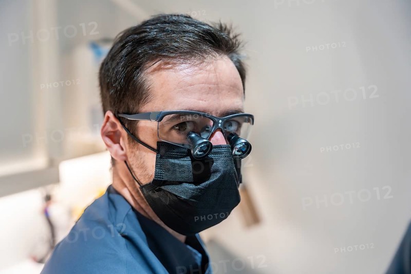 Dentist wearing surgical loupes and a mask is skillfully performing dental procedures in a modern dental clinic, ensuring patient care and hygiene